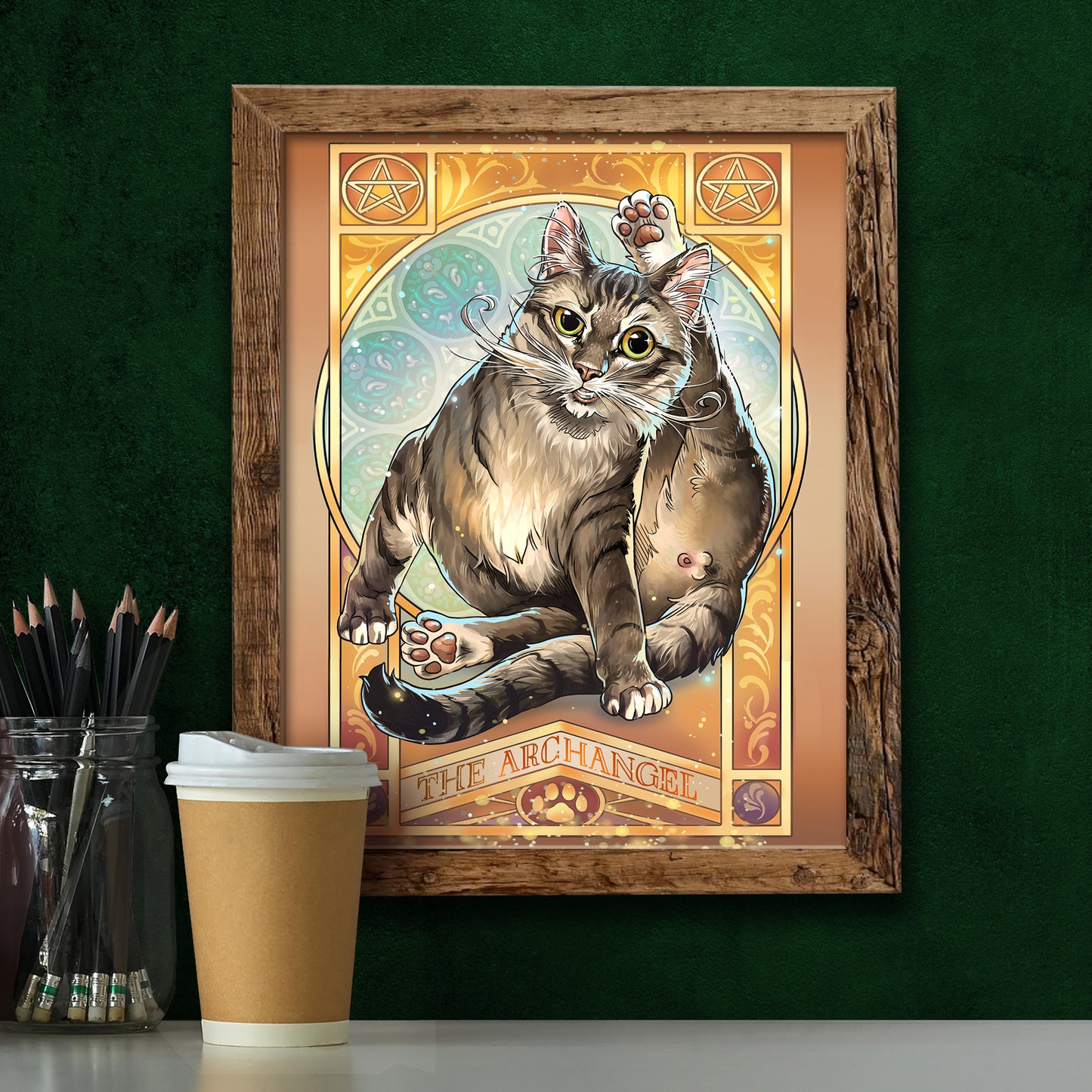 Framed artwork of a cat titled 'The Archangel' on a green wall with a coffee cup and pencils.