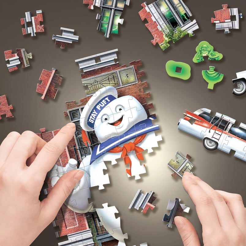 Jigsaw puzzle pieces depicting the firehouse headquarters from the "Ghostbusters" movies. A model's hand is putting the pieces together.