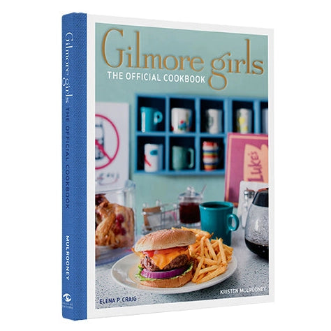 A mint green cookbook with a blue spine set against a white background. The book cover reads "Gilmore Girls: The Official Cookbook" and features a plate of burgers and fries sitting in a vintage-style diner.