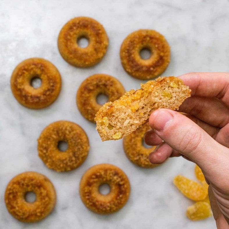Load image into Gallery viewer, Freshly-baked doughnuts on a marble tabletop. A model&amp;#39;s hand holds half a doughnut, showing the fluffy interior.
