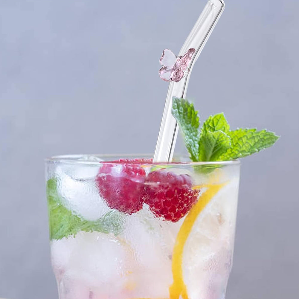 Close up of a tall glass filled with a clear beverage and cherries. A glass drinking straw is sticking out of the top, with a small purple glass butterfly attached at the straw's bend point. 