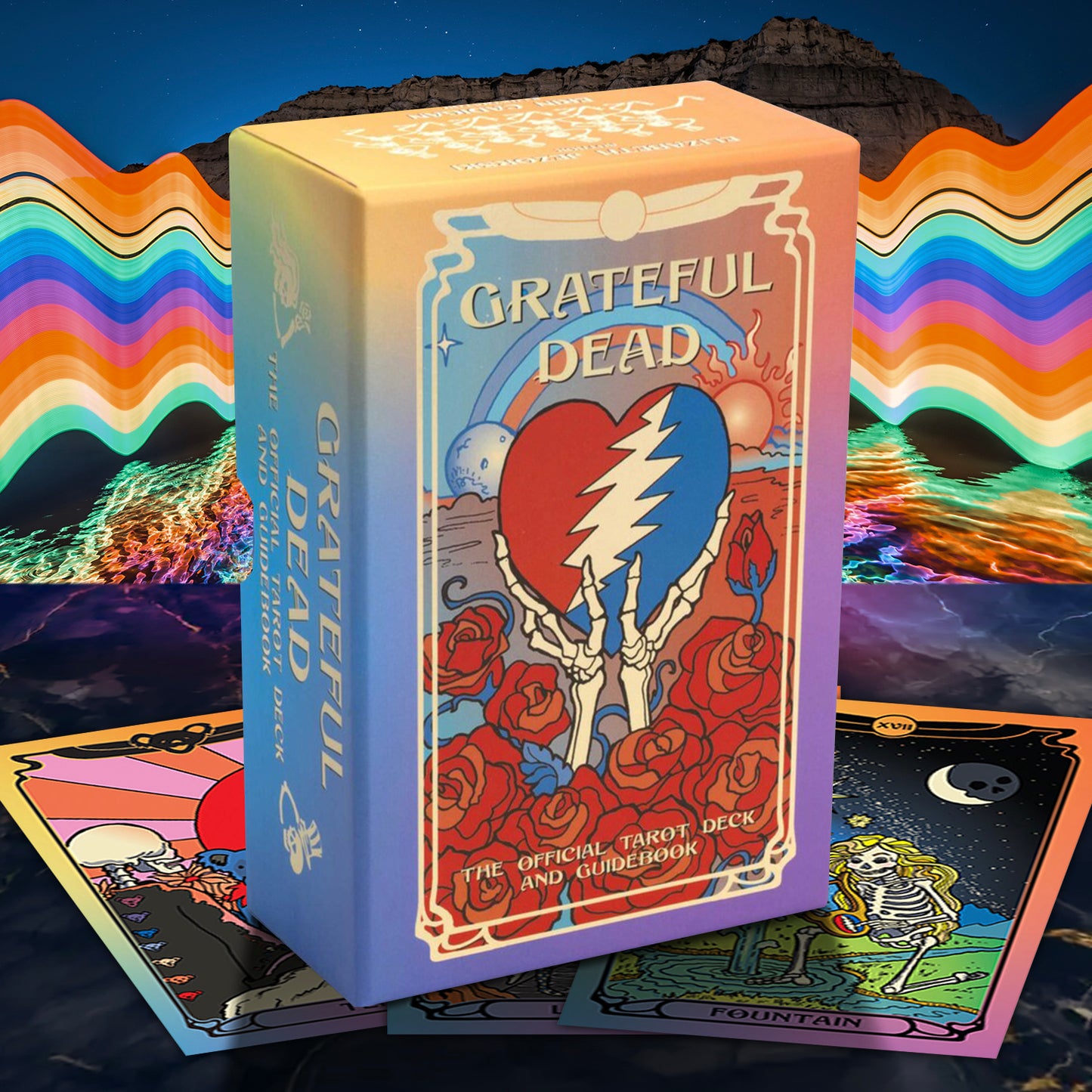 Grateful Dead tarot card deck box with colorful Grateful Dead artwork, shown with several tarot cards fanned out in front against a psychedelic rainbow and mountain background.