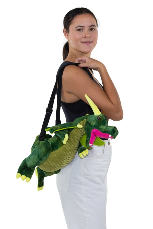 A female model carrying a green dragon-shaped backpack on her shoulder. The dragon has black carrying straps on its back.