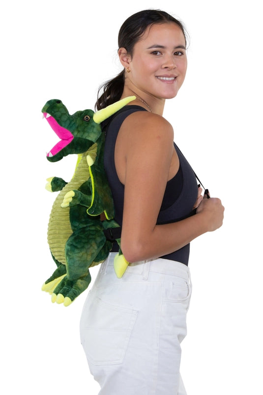 A female model wearing a green dragon-shaped backpack on her shoulders. The dragon has black carrying straps on its back.