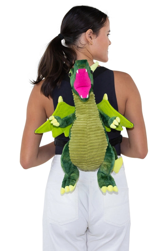 A female model wearing a green dragon-shaped backpack on her shoulders. The dragon has black carrying straps on its back.