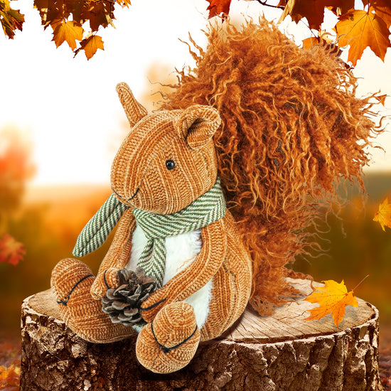 A stuffed squirrel with a bushy orange tail, sitting on a tree stump in a forest. The squirrel is wearing a green and white striped scarf, and is clutching a pine cone in its front paws.