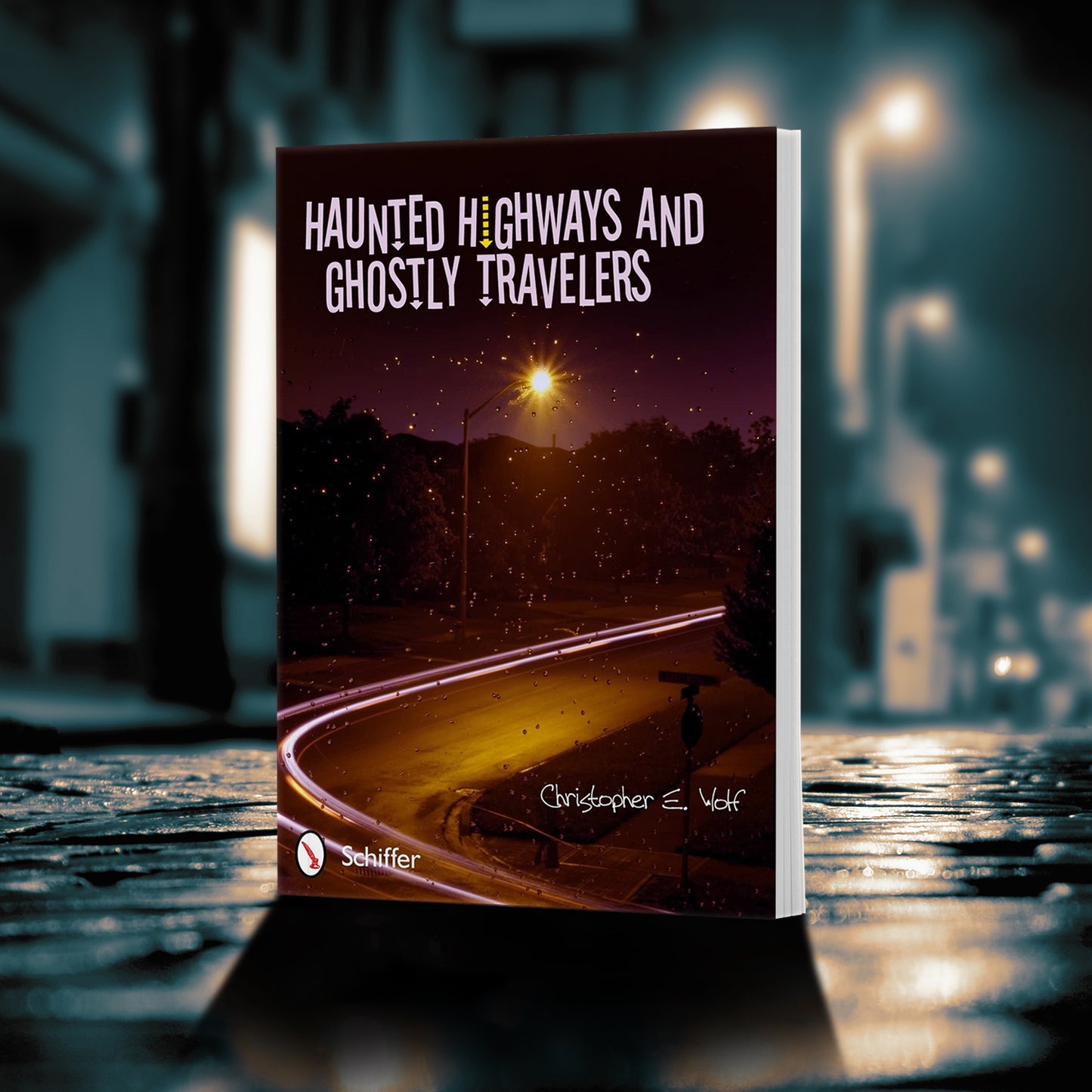 An image of a book standong on a dimly lit street. The cover image depicts a rainy street at night. At the top in white text is "haunted highways and ghostly travelers." 