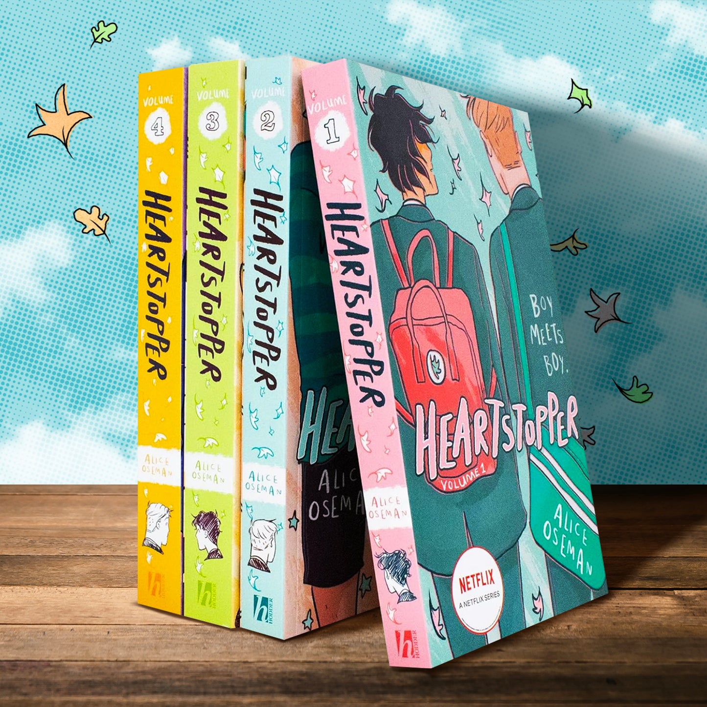 The first 4 volumes of 'Heartstopper', spines out, on a wooden table. The books are in front of a cloudy background illustrated with the classic Heartstopper leaves