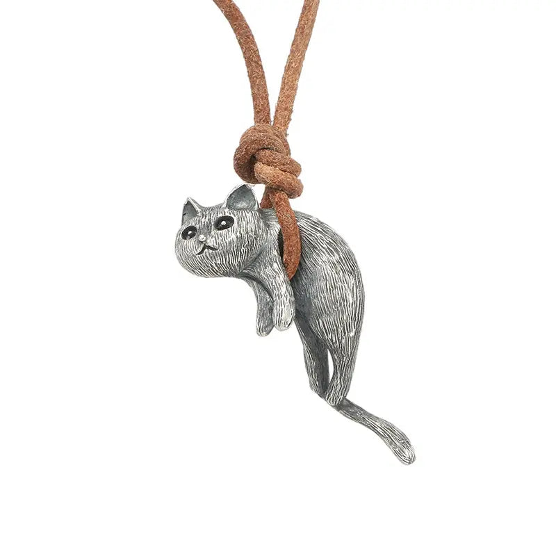 Close up of a cat-shaped pendant hanging from a brown leather cord, against a white background. The cord is wrapped under the cat's abdomen, suspending it in mid-air.