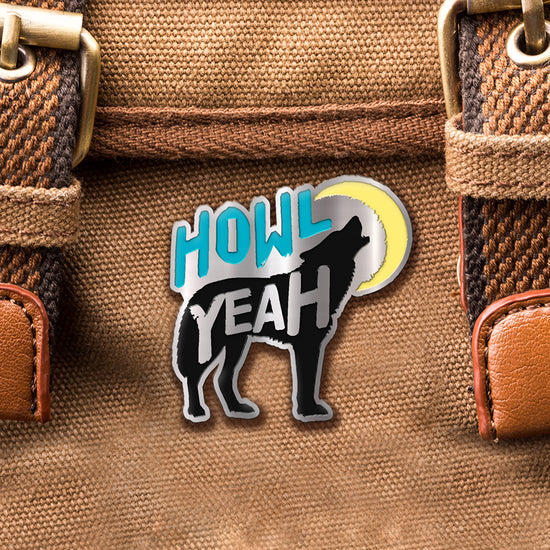 Load image into Gallery viewer, A brass pin with &amp;quot;howl&amp;quot; (blue), &amp;quot;yeah&amp;quot; and a howling wolf (black) with a yellow moon. The pin is affixed to a brown canvas bag.
