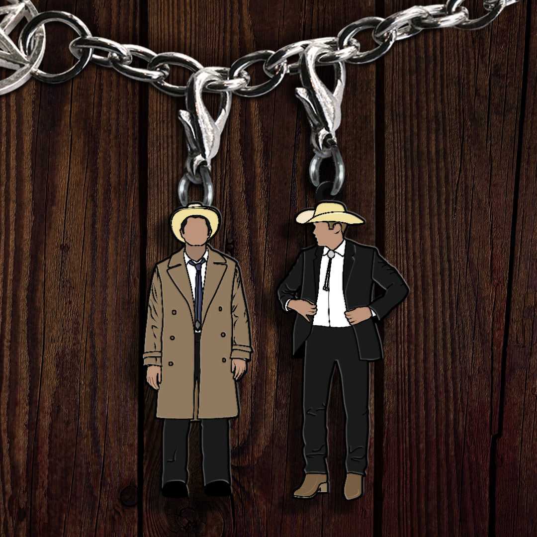 A pair of charms depicting Dean Winchester and Castiel dressed in western outfits., on a wooden background