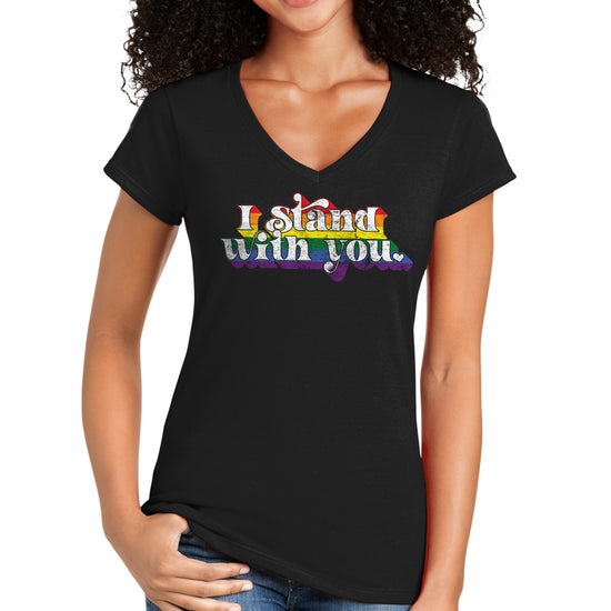 A female model wearing a black T-shirt with "I Stand With You" in white letters. The letters are bordered by lines in the colors of the rainbow.