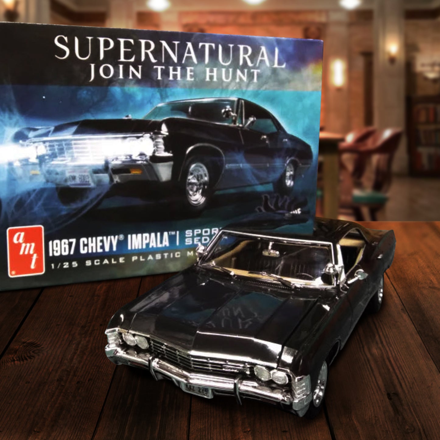 A model kit box depicting Baby, the 1967 Chevy Impala from the TV series "Supernatural," against a dark forest in the background. White text at the top says "Supernatural, join the hunt." White text at the bottom describes the kit. The box is sitting on a wooden table in The Bunker. Next to the box is the completed car model.