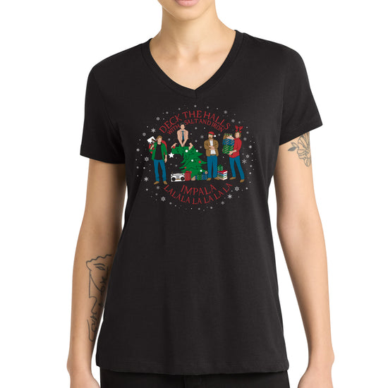 A model in a black v-neck tee, with a Supernatural themed holiday design on the front. Red text says "deck the halls with salt and iron. Impala lalala la la lala."