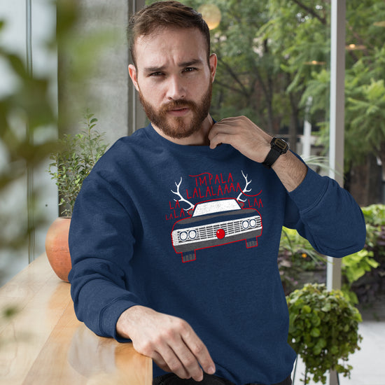 A bearded man in a navy crewneck sweatshirt. The sweatshirt reads "Impala-la-la-laaa" in red capital font, above a front-facing view of a vintage Impala "wearing" a red nose in the front grill and white antlers coming out of the roof.