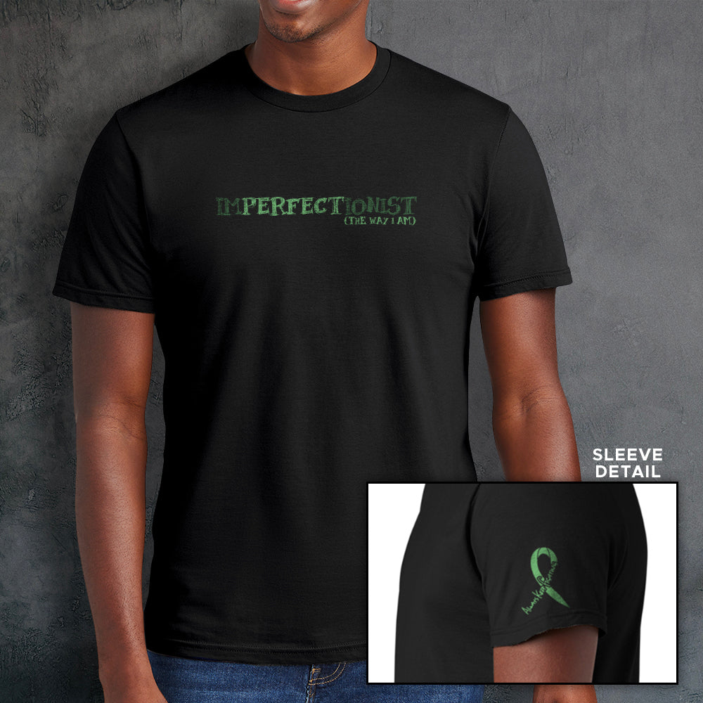 A male model wearing a black t-shirt. The front reads "IMPERFECTIONIST". The word "perfect" is printed in a darker shade, and the words "the way I am" are printed beneath it, so the full impression reads 'Imperfectionist / Perfect the way I am" . The sleeve bicep has a green ribbon that reads "always keep fighting" within it.