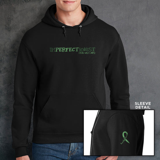 A male model wearing a black pullover hoodie. The front of the hoodie reads "IMPERFECTIONIST". The word "perfect" is printed in a darker shade, and the words "the way I am" are printed beneath it, so the full impression reads 'Imperfectionist / Perfect the way I am" . The sleeve bicep has a green ribbon that reads "always keep fighting" within it.