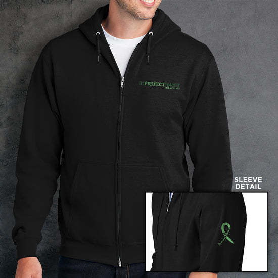 A male model wearing a black zip hoodie. The front reads "IMPERFECTIONIST" on the breast "pocket area". The word "perfect" is printed in a darker shade, and the words "the way I am" are printed beneath it, so the full impression reads 'Imperfectionist / Perfect the way I am" . The sleeve bicep has a green ribbon that reads "always keep fighting" within it.