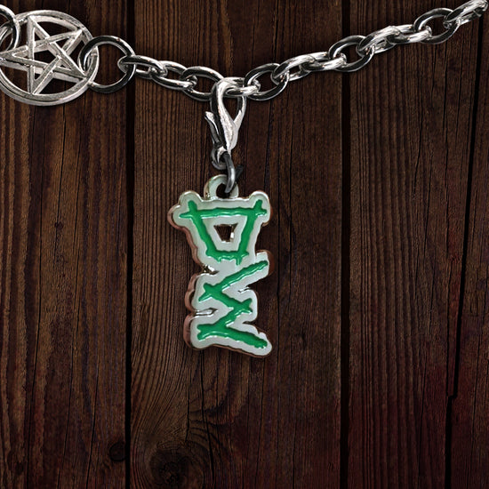 A metal charm on a linked bracelet, against a dark wooden background. The charm depicts the initials DW in green. At the top left is a charm with the anti-possession symbol at its center.