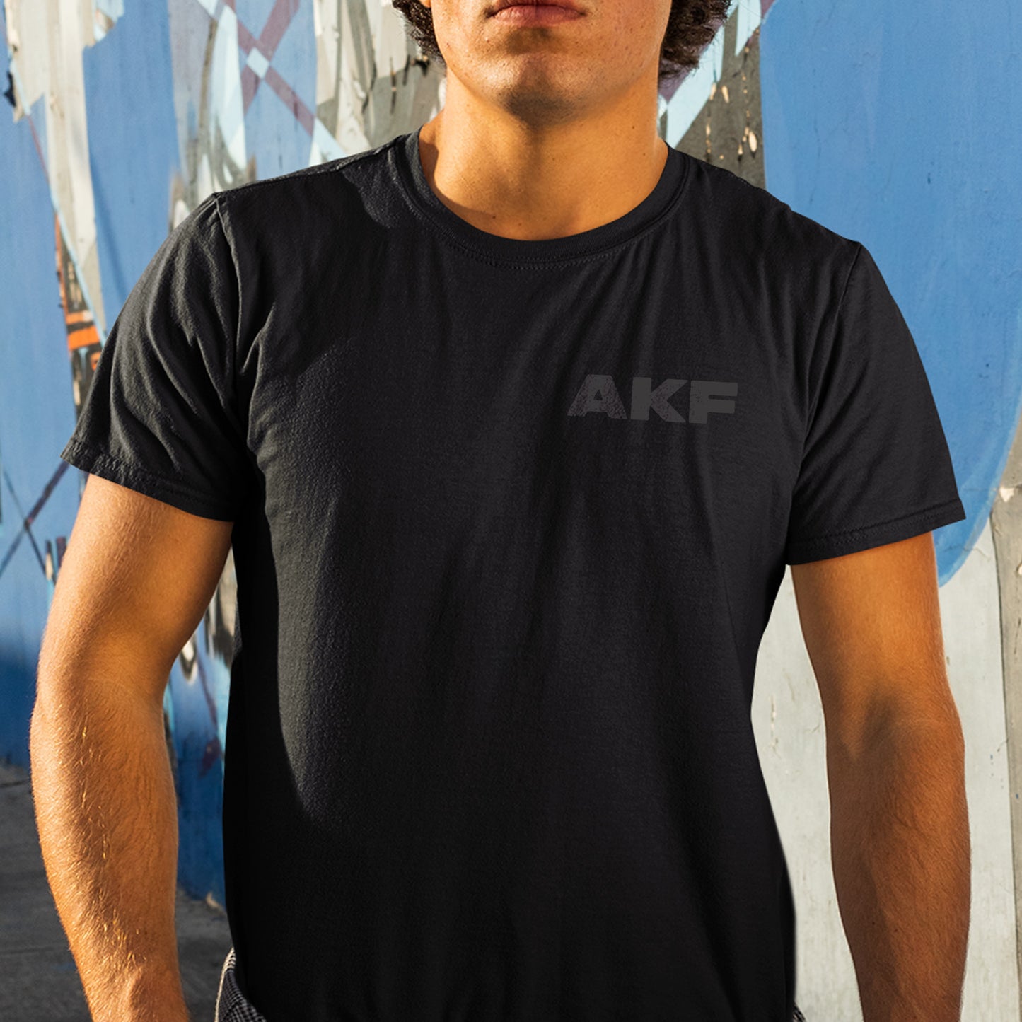 Person wearing a black t-shirt with 'AKF' logo against a colorful wall.