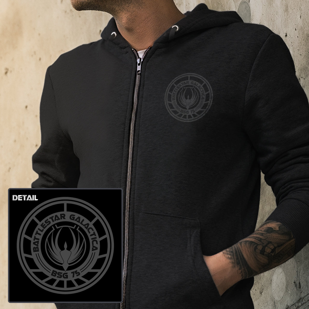 Person wearing a black hoodie with a Battlestar Galactica logo, with a close-up detail of the logo on the left.