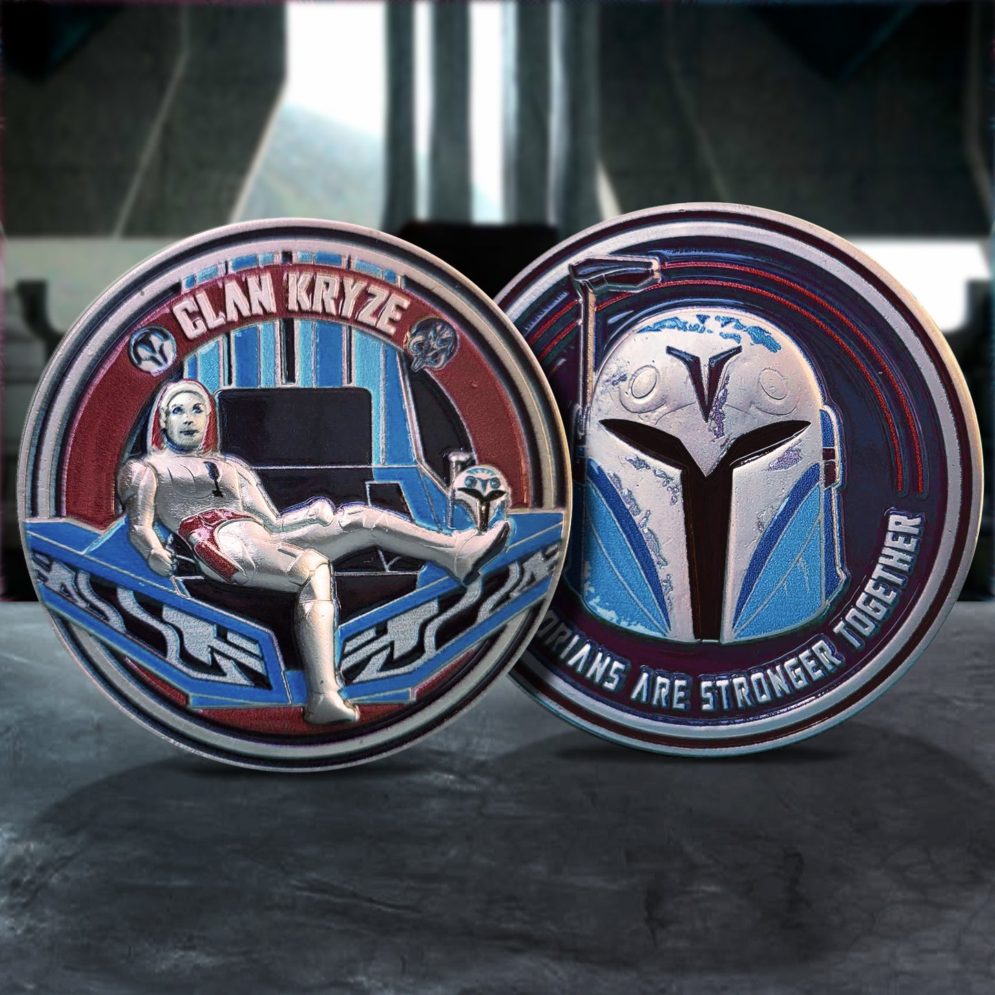 Side by side images of a metal challenge coin, on a dark grey table. The left coin depicts Bo Katan on a throne, with Clan Kryze" in silver text at the top. The right coin depicts Bo Katan's helmet against a blue background, with silver text at the bottom that says "Mandalorians are stronger together."