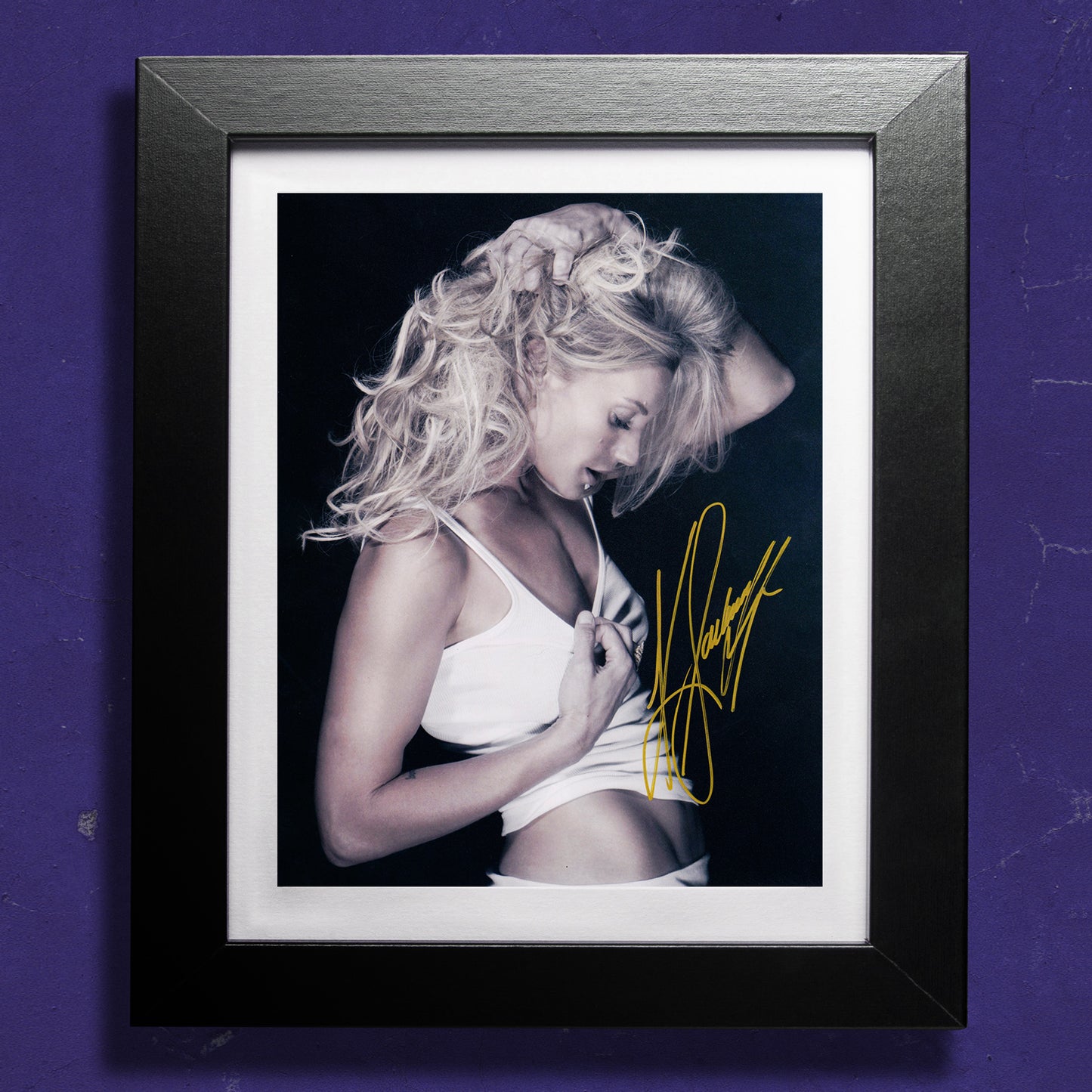 A framed image against a purple wall. The image shows actor Katee Sackhoff in a white tank top, clutching her hair. Across the front of the image is Katee's autograph.