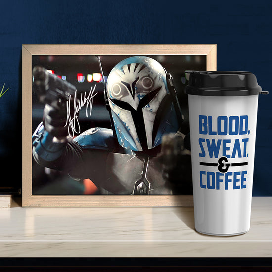 A framed picture of Katee Sackoff's character from The Mandalorian TV series, in full armor. In the corner of the image is Katee's autograph. In front of the framed picture is a white travel mug with blue text that says "blood, sweat & coffee."