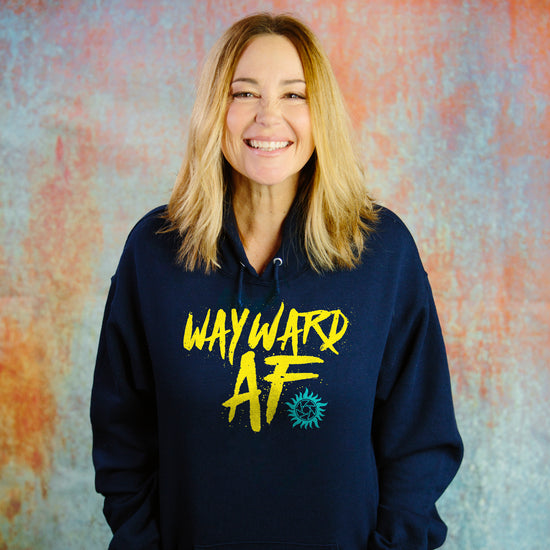 An image of actor Kim Rhodes wearing a navy blue pullover hoodie. Printed on the front are the words "WAYWARD AF" in a bright yellow handwriting-like font, with a small light blue anti-possession symbol