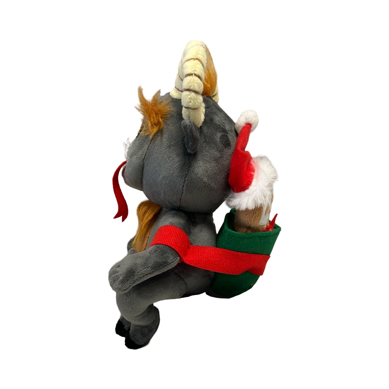 Side view of a grey plushie depicting the mythological figure Krampus. At the top of his head are yellow horns and patches of brown hair. Across his face are white fangs, and a long red tongue. A small gingerbread figure wearing a santa hat is on the plushie's back.