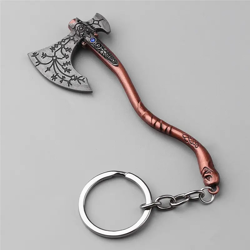 A key chain shaped like Leviathan Axe used by Kratos in the God of War video game series, against a grey background. The axe handle is a dark rose gold color, with an S-shaped curve, and a key ring attached at the end. The axe head is dark grey with runes carved into the blade. A blue jewel sits in the center of the axe head.