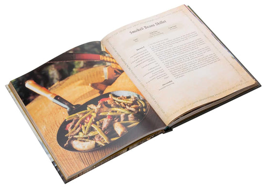 A bird's eye view of the opened cookbook, with two pages visible. On the left is an iron skillet with beans and sausage cooking. On the right is a recipe for Smoked Beans Skillet.