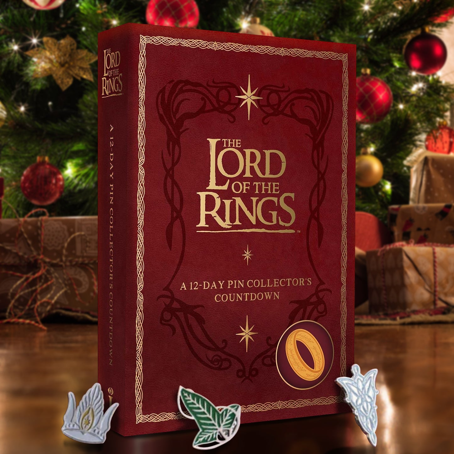 A dark red box in front of a decorated Christmas Tree. The front has gold text that says "the lord of the rings. a 12 day pin collector's countdown." In front of the box are Lord of the Rings themed pins.