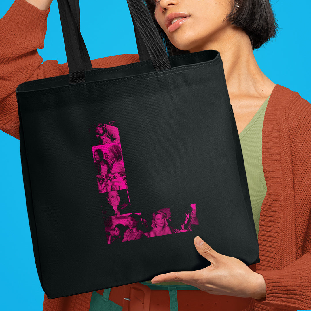 A model in a green shirt and dark orange sweater holding a black tote bag. On the front of the bag is a pink letter L. Inside the L are pink and black images of characters from the TV series The L Word.