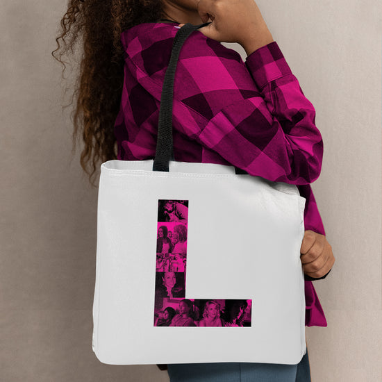 A model in a pink plaid shirt carrying a white tote bag. On the front of the bag is a pink letter L. Inside the L are pink and black images of characters from the TV series The L Word.