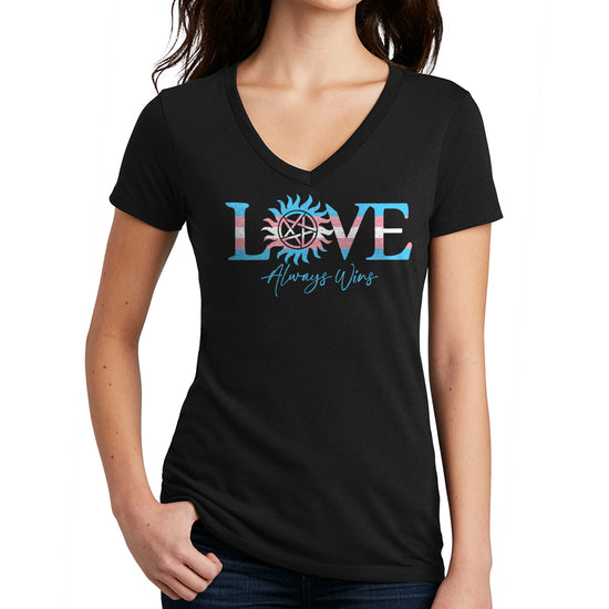 A female model wearing a black T-shirt. At the center is text saying "LOVE Always Wins." The "O" is in the shape of a Sun, with a pentagram at the center. "Love" is in the colors of the Transgender Pride flag, in light blue, white, and pink. "Always Wins" is in script text, printed in blue beneath "Love."