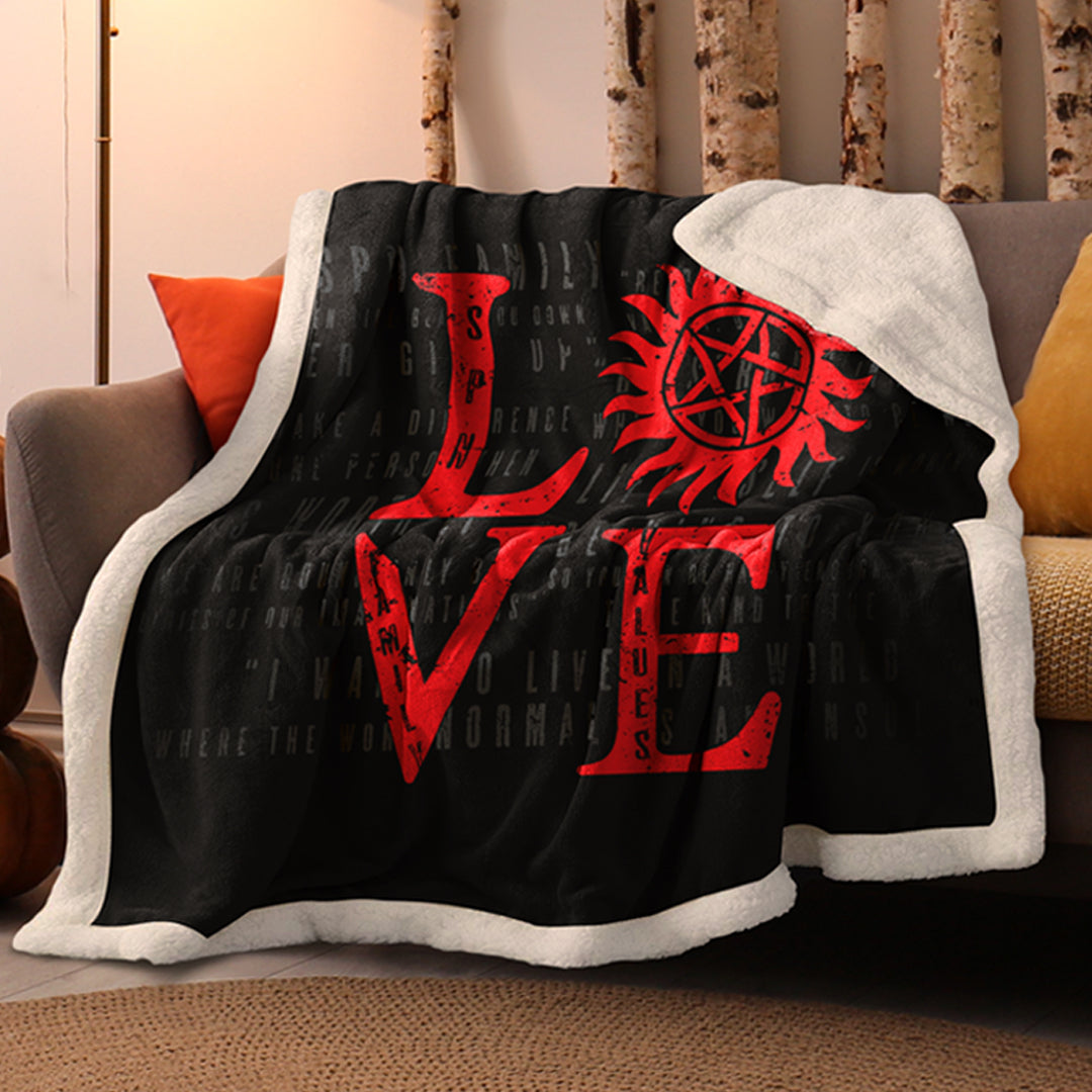 A black blanket with a white border, slung over a grey sofa. On the blanket is the word "love" in red, with the "O" replaced by the anti-possession symbol.