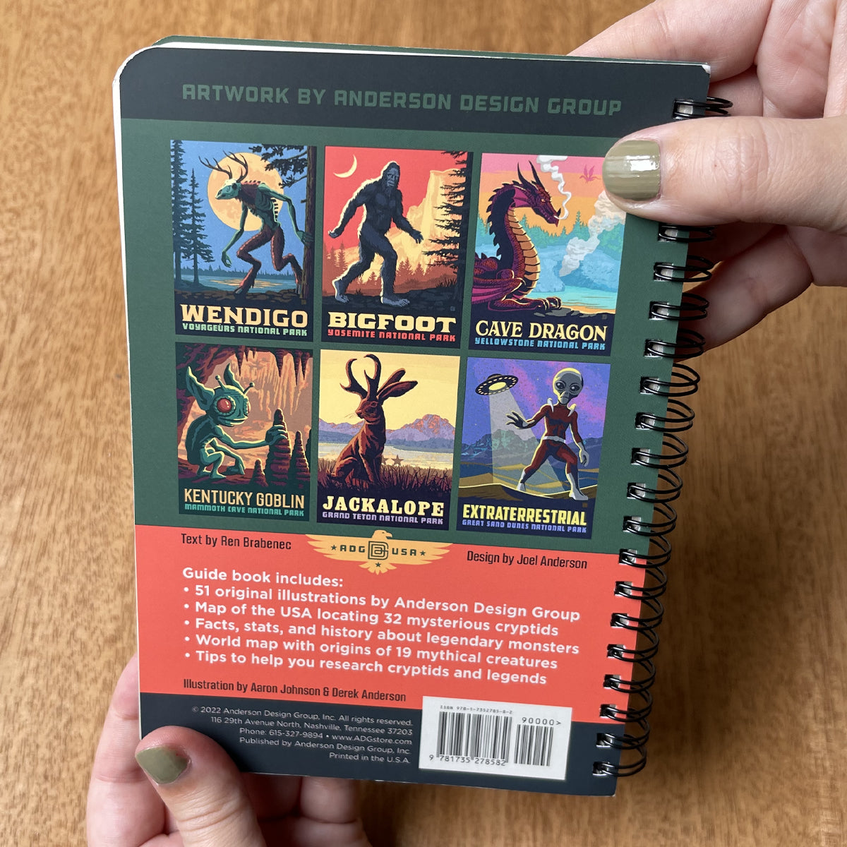 Notebook with illustrations of mythical creatures held by a person on a wooden surface