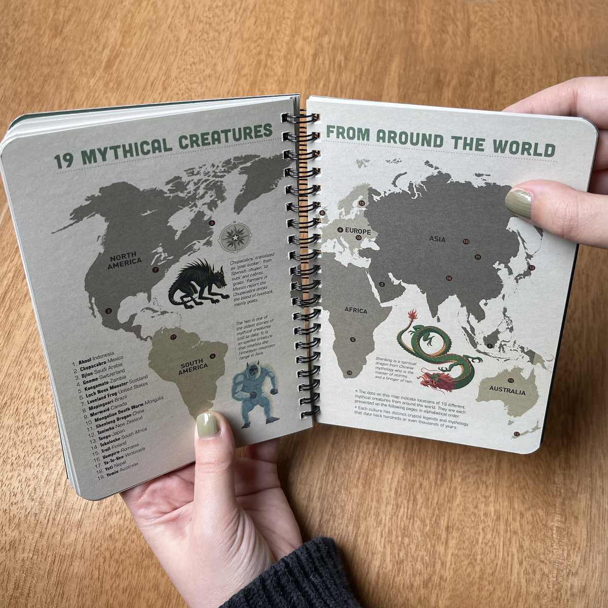 Open notebook with world map and mythical creatures on a wooden surface