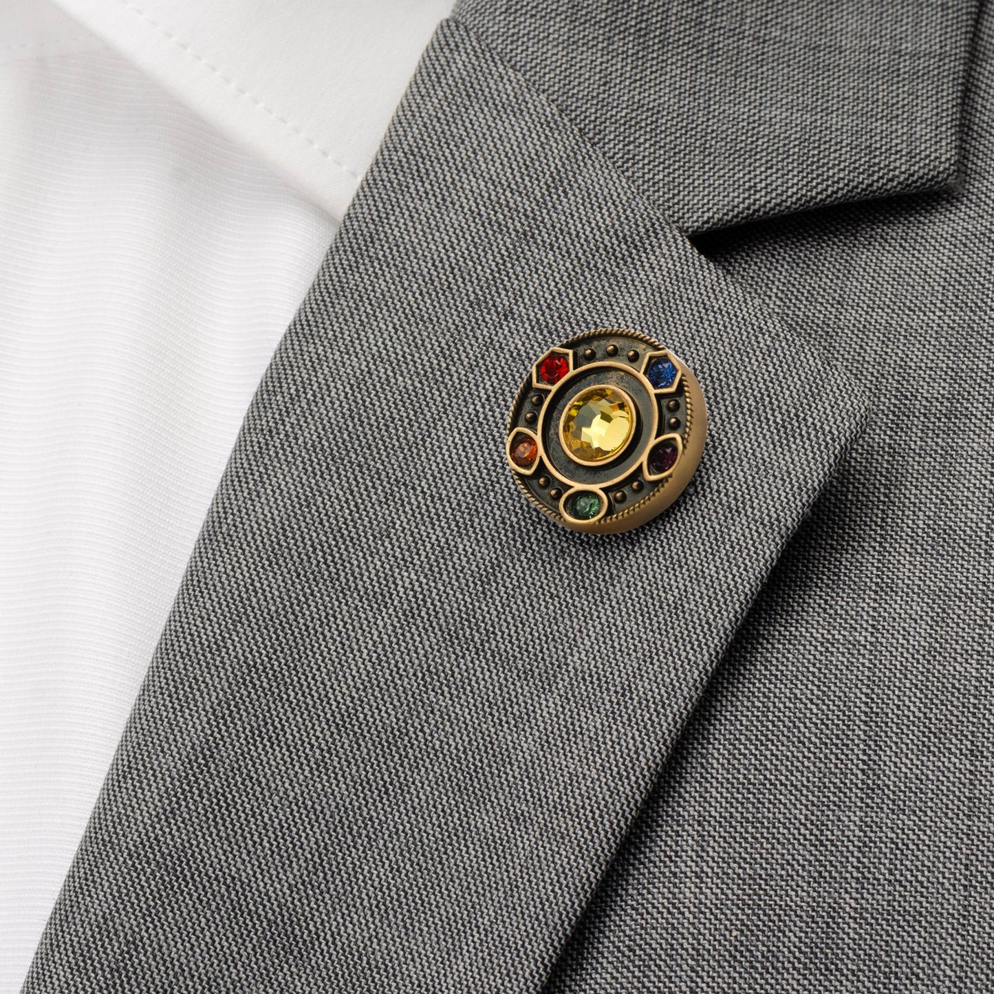 Gold lapel pin depicting the Marvel infinity stones on a grey suit jacket