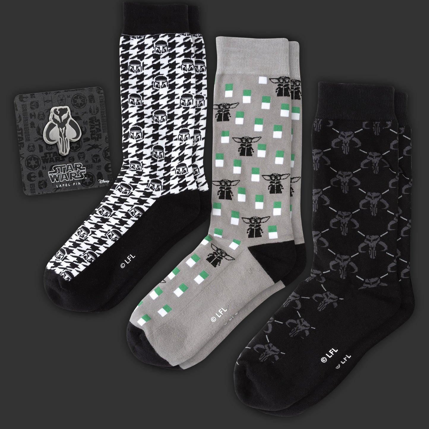 Three pairs of Mandalorian-themed socks on a dark background. Next to them is a Mandalorian pin on a black cardboard backing.