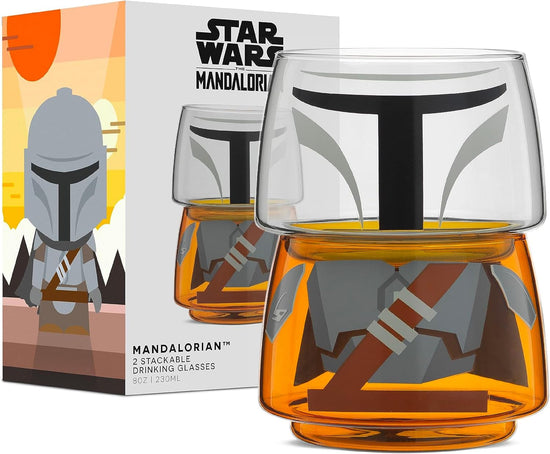 Two small drinking glasses stacked on each other against a white background. The two glasses combined depict the titular character from the Star Wars series The Mandalorian. Next to the glasses is a cardboard box, depicting the set.