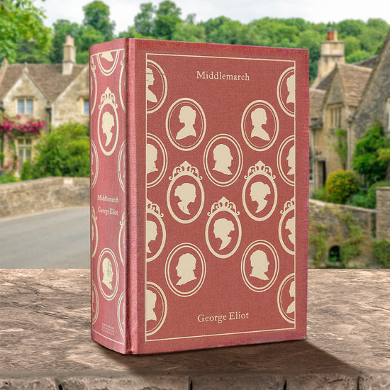 A pale red hardcover book standing on a stone fence.  A pattern of cream-colored cameos is printed across the cover. At the top is cream-colored text that says "Middlemarch." In the background are old stone houses next to a road.