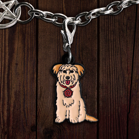An enamel charm on a wooden background. The charm is shaped like a light brown shaggy dog, with a red color around its neck. Attached to the collar is a tag in the shape of the anti-possession symbol.