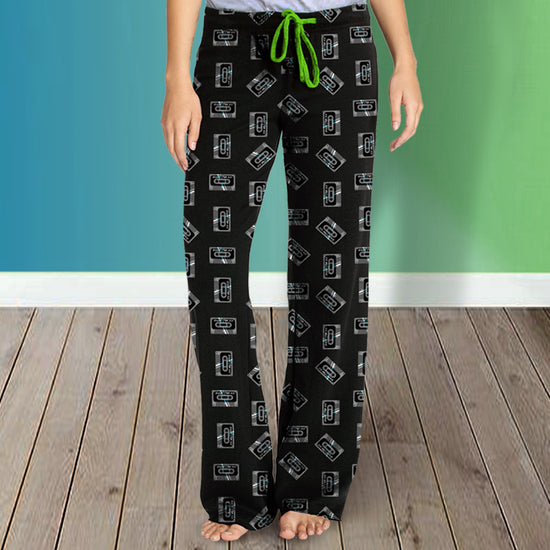 A pair of pajamas pants with a green tie string and covered in "mix tapes" - the mix tape is a cassette tape that says "Zepp Traxx" on it. Behind the model is a green and blue background.