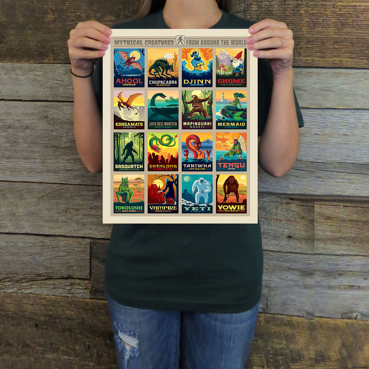 Person holding a poster with various mythical creature illustrations against a wooden background