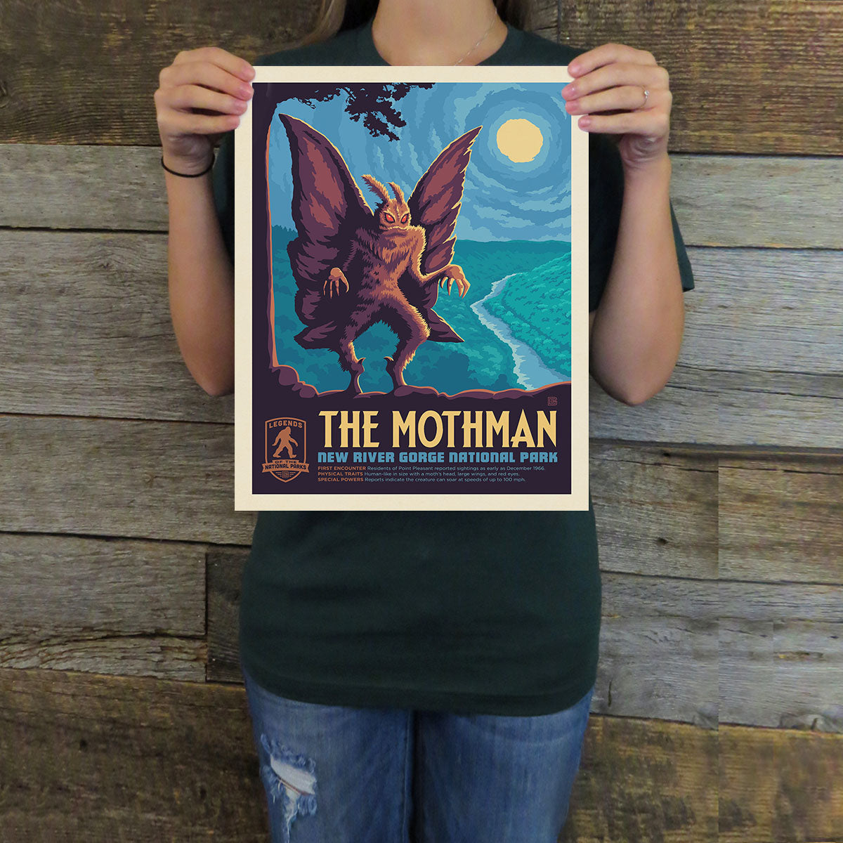 Person holding a Mothman poster against a wooden background