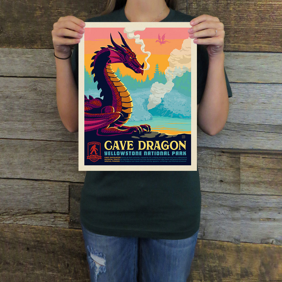 Person holding a 'Cave Dragon' Yellowstone National Park poster against a wooden background