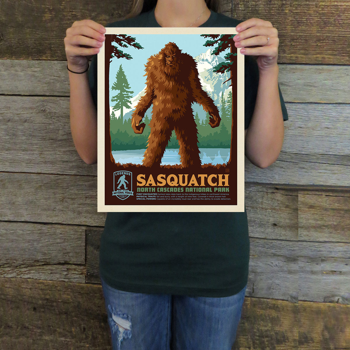 Person holding a Sasquatch-themed poster against a wooden background