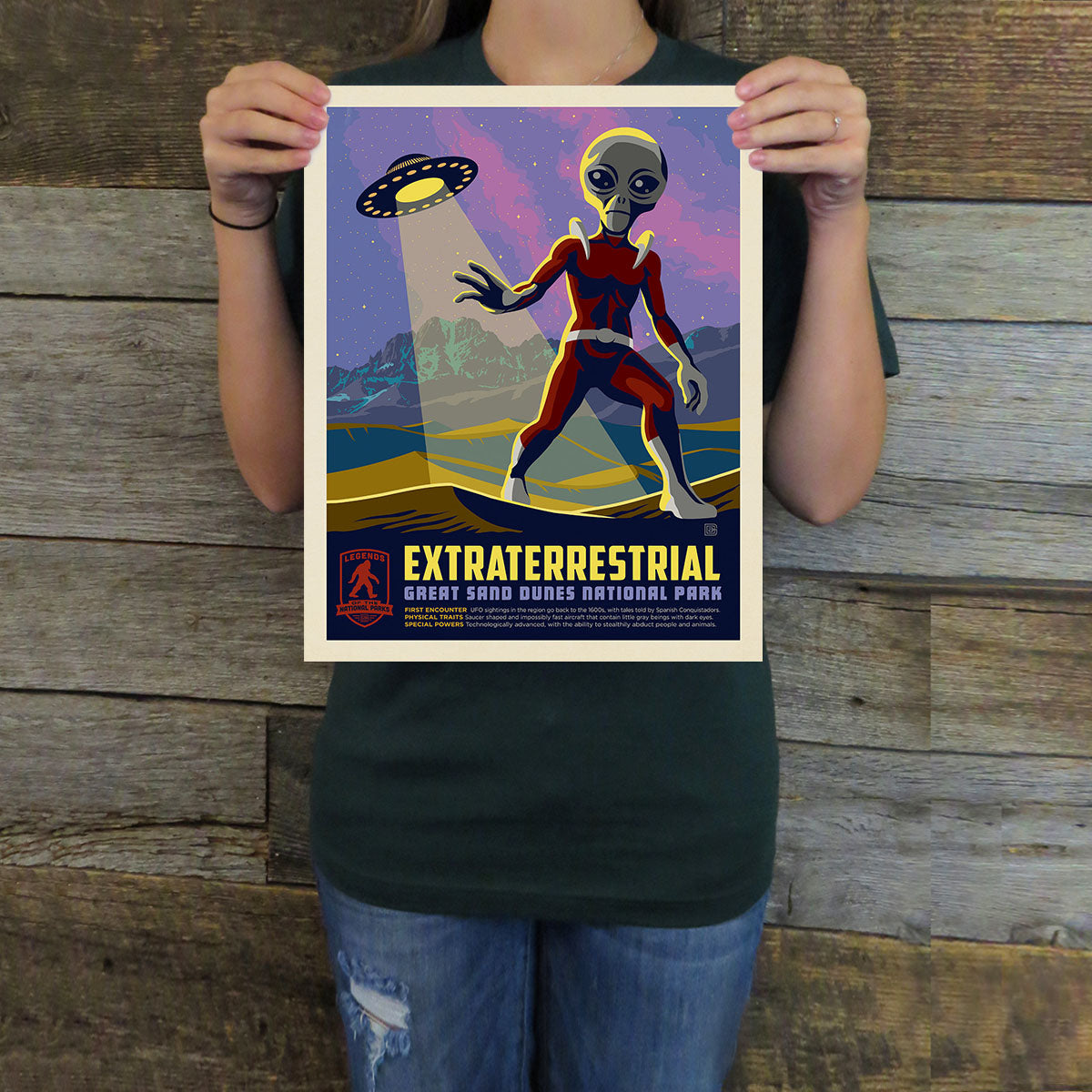 Person holding a poster with an alien design against a wooden background